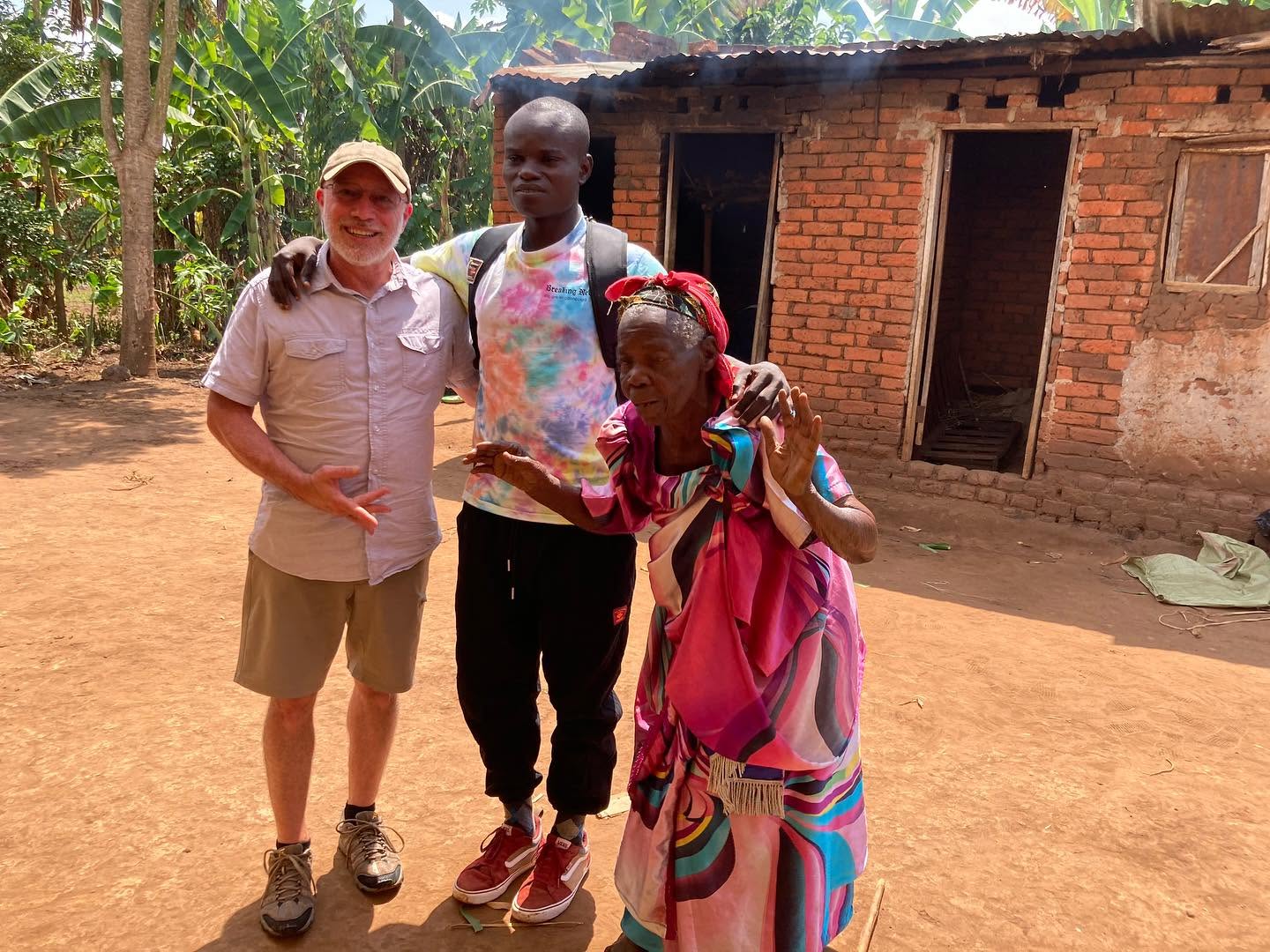 A visiting team member stands with a young man and an older woman in prayer outside a home