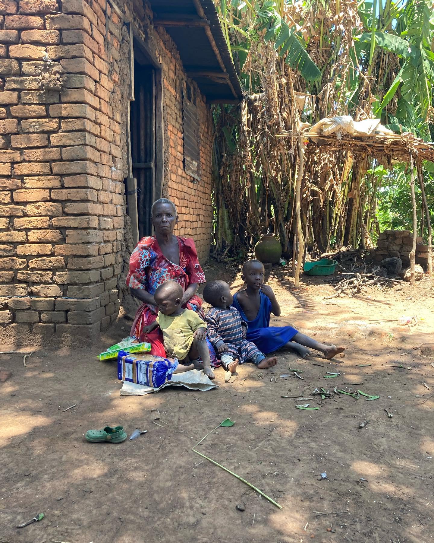 An older caregiver sits with three young children outside a brick home